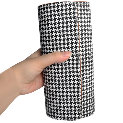 Luxury watch roll organiser for multiple watches. Hand holding a cylindrical black and white houndstooth patterned product against a white background