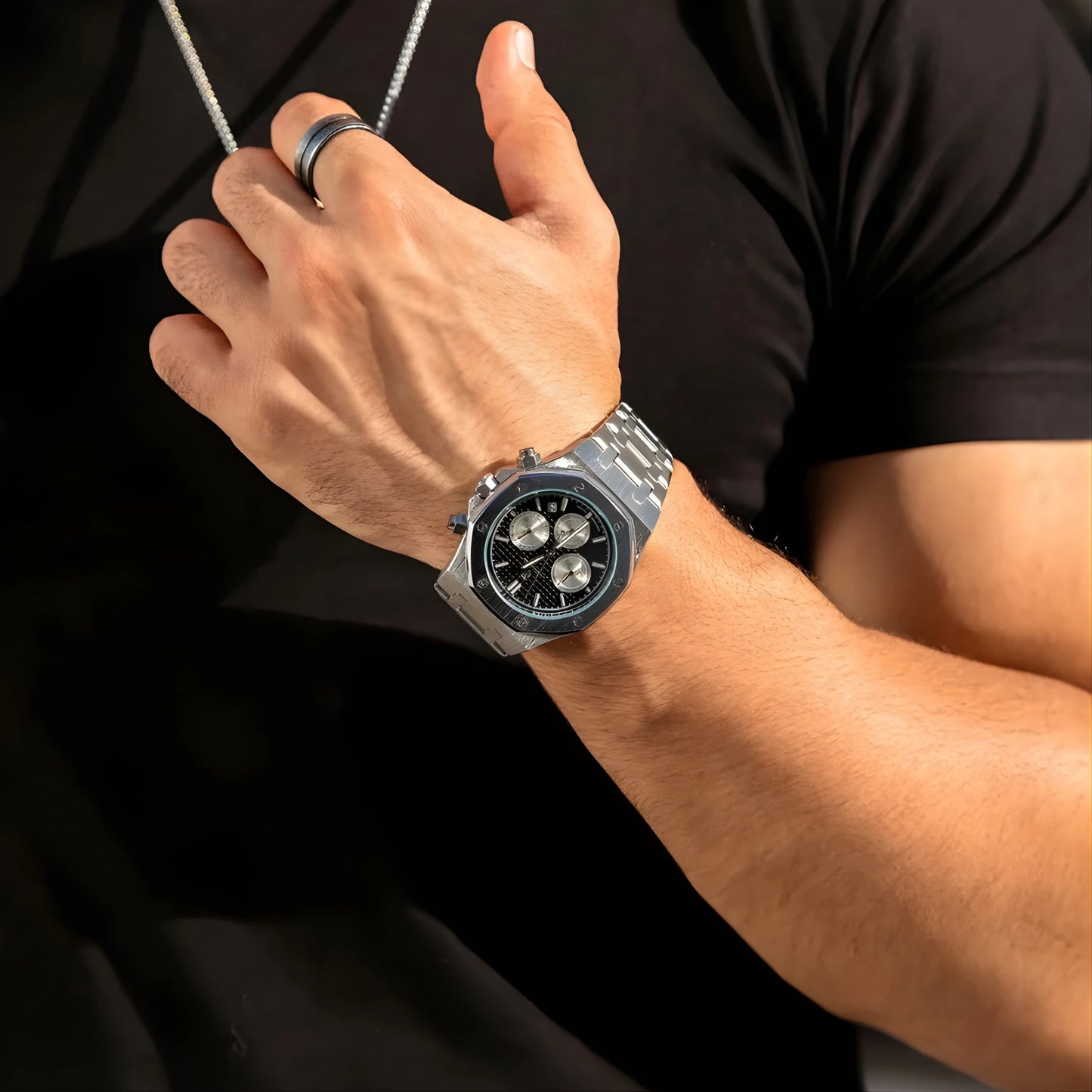 Close-up of a person's wrist wearing a silver watch with a black face on a dark background